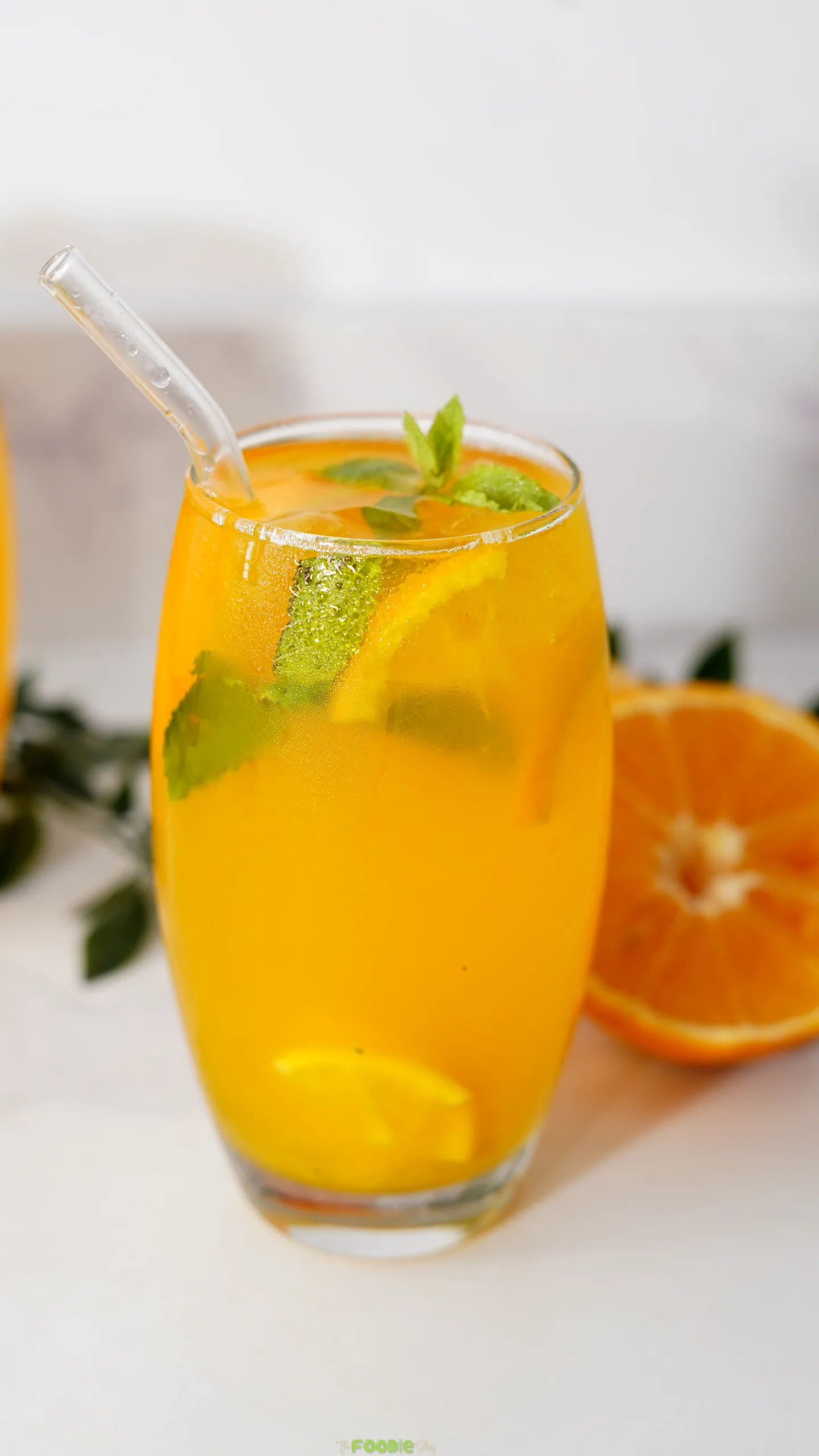 Cold orange vodka mojito with fresh mint, citrus slices, ice, and a glass straw.