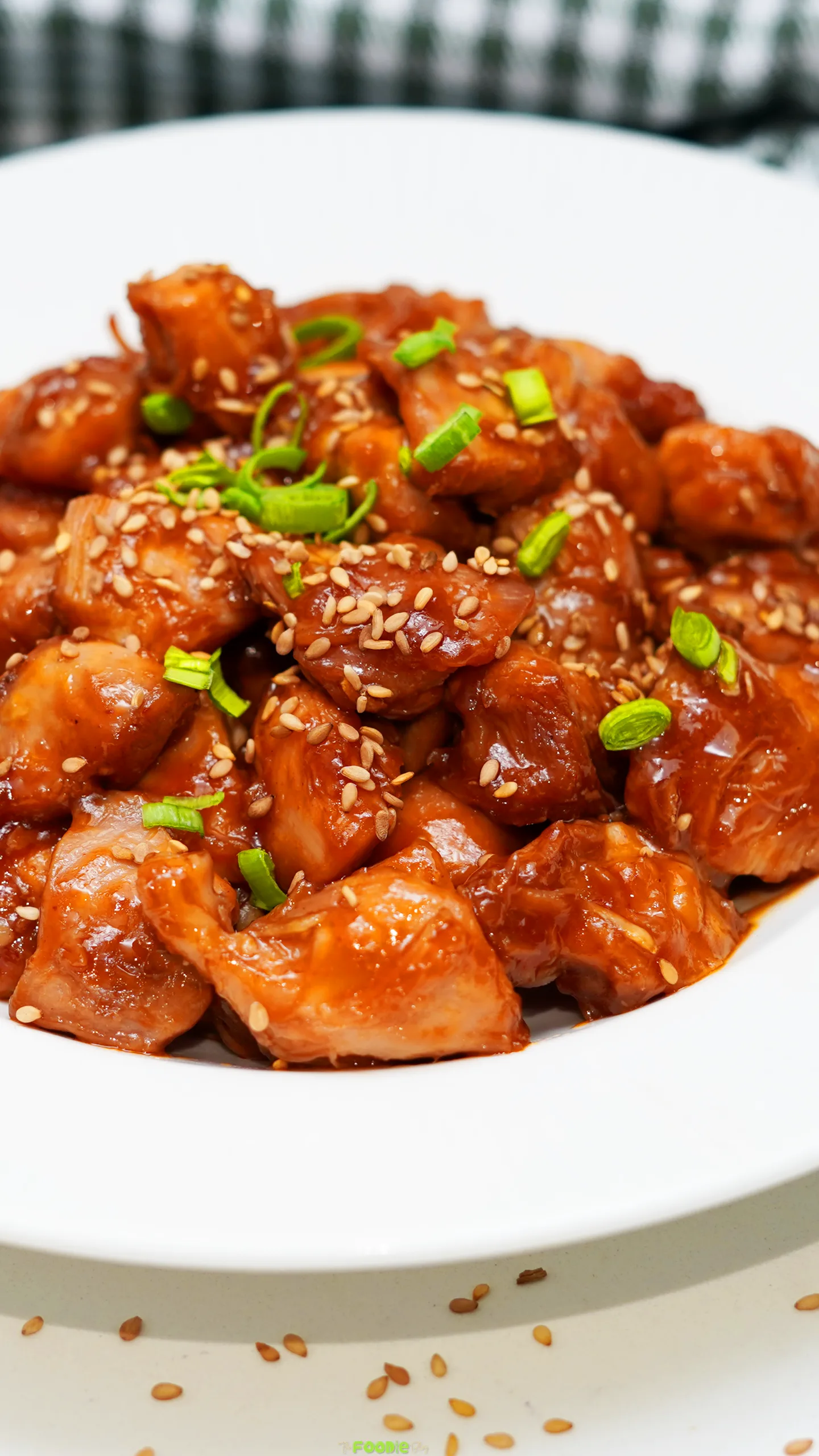 Close-up of sticky chicken thigh pieces coated in honey soy sauce with sesame seeds and green onions.