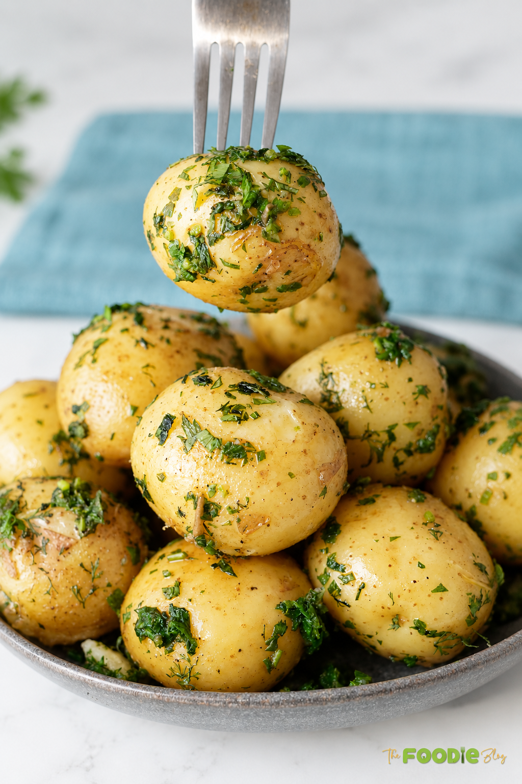 Baby potato coated with melted butter, fresh dill, parsley, and chives lifted with a fork above a bowl of herb potatoes.