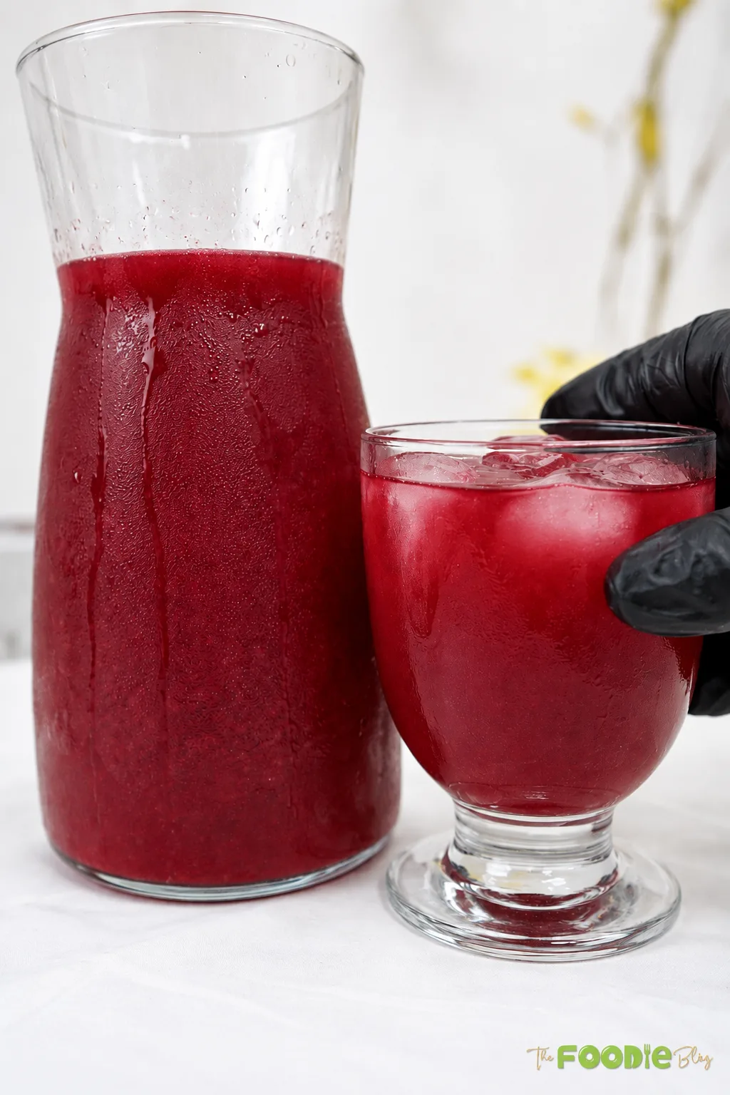 Cold homemade beetroot juice served over ice in a glass with a chilled pitcher in the background.