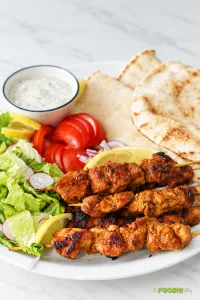 Grilled chicken skewers served with pita bread, lettuce, tomatoes, lemon, and creamy herb sauce.