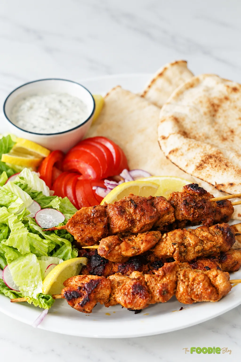 Grilled chicken skewers served with pita bread, lettuce, tomatoes, lemon, and creamy herb sauce.