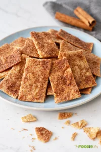 Crispy cinnamon sugar tortilla chips piled on a blue plate with cinnamon sticks in the background.
