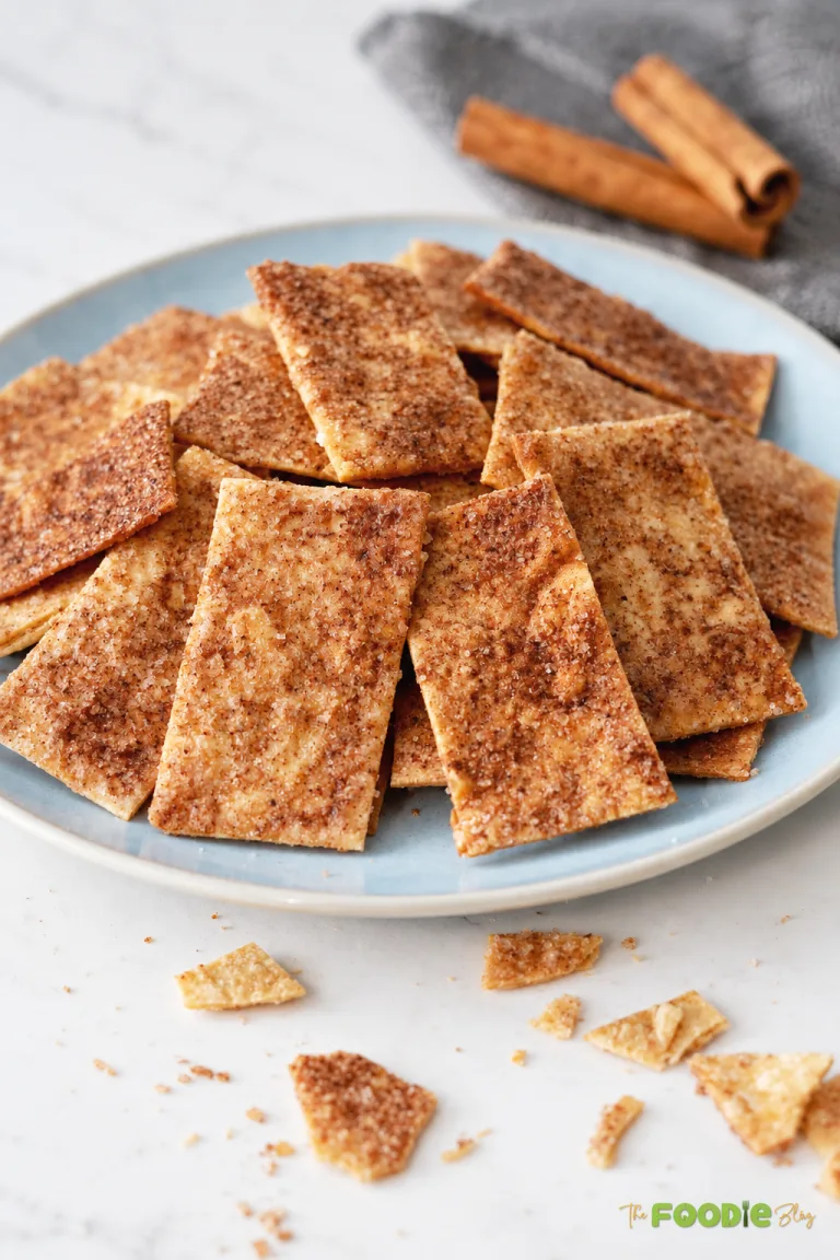 Crispy cinnamon sugar tortilla chips piled on a blue plate with cinnamon sticks in the background.