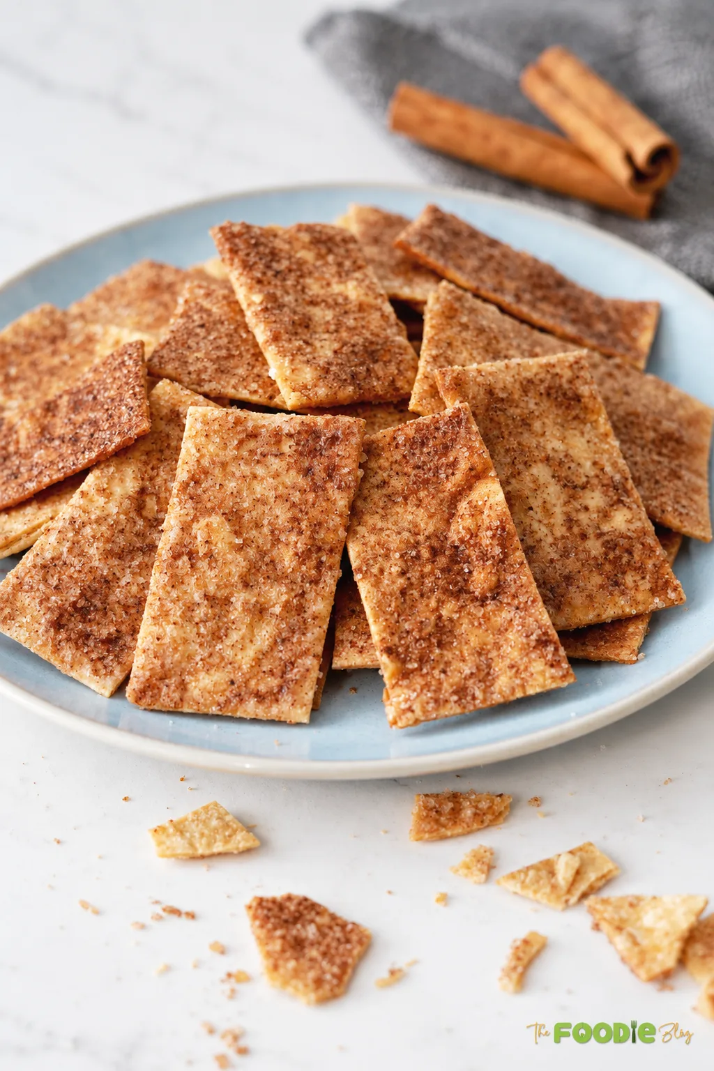 Crispy cinnamon sugar tortilla chips piled on a blue plate with cinnamon sticks in the background.