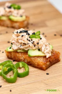 Crispy rice with spicy tuna, avocado, jalapeño, and black sesame seeds on a wooden board.