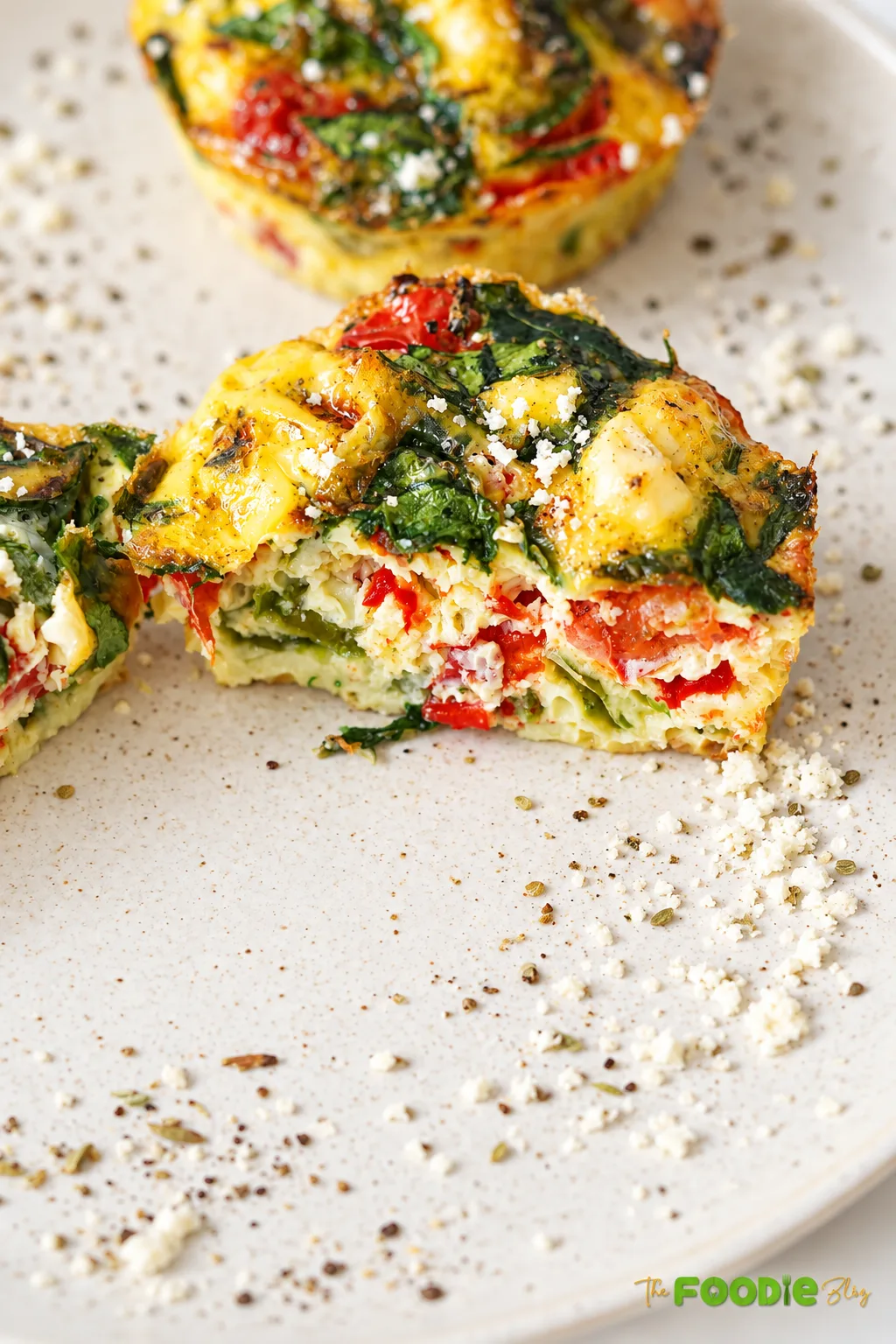 Spinach tomato feta egg muffin cut open to show the fluffy vegetable-filled center.