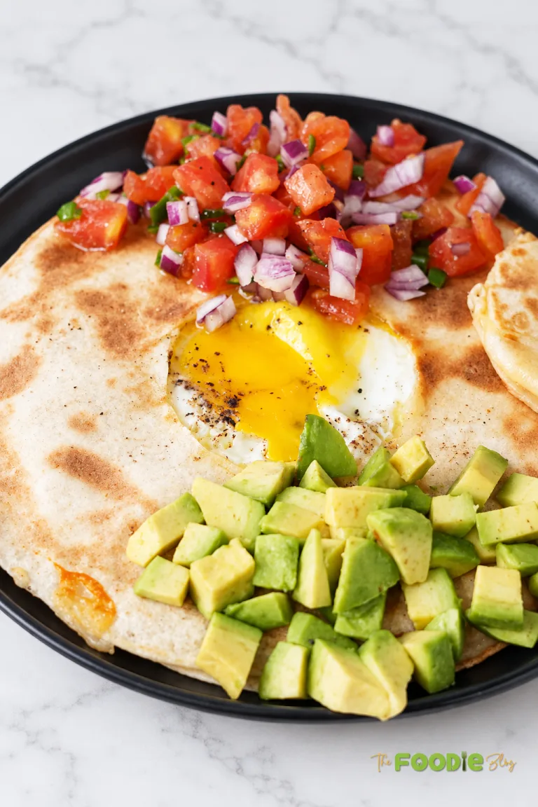 Egg quesadilla served with avocado, tomato salsa, red onion, and jalapeño on a black plate.
