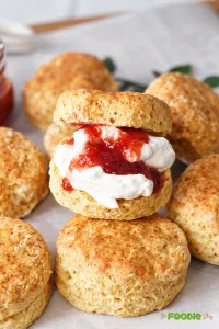 English scone split and filled with whipped cream and strawberry jam surrounded by freshly baked scones.