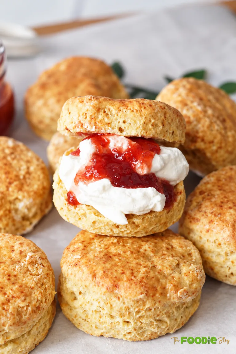 English scone split and filled with whipped cream and strawberry jam surrounded by freshly baked scones.