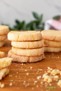 French sablé cookies stacked on a wooden board with crisp sugar-coated edges.