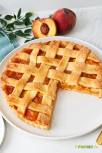 Fresh peach pie with a golden lattice crust and juicy peach filling served on a white plate.