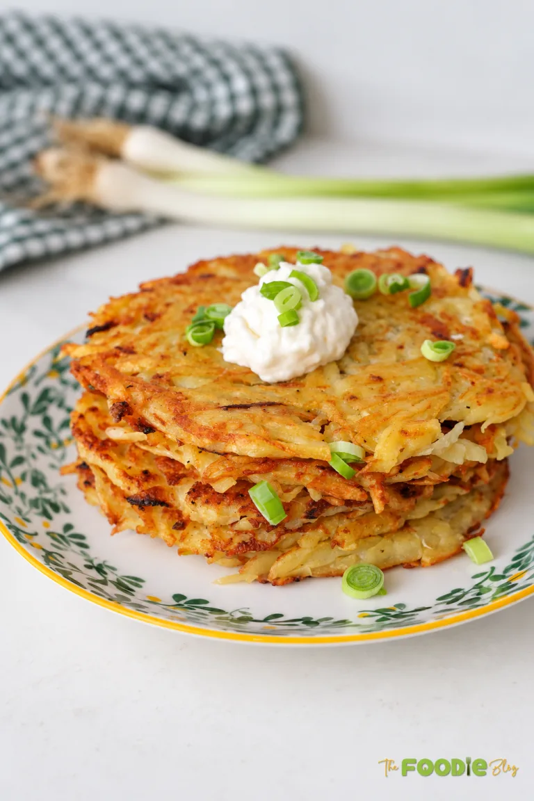 Crispy German potato pancakes stacked on a plate with sour cream and sliced green onions.