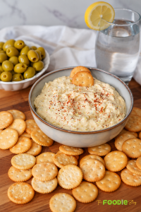 Creamy green olive dip served with crackers, green olives, and a glass of lemon water.