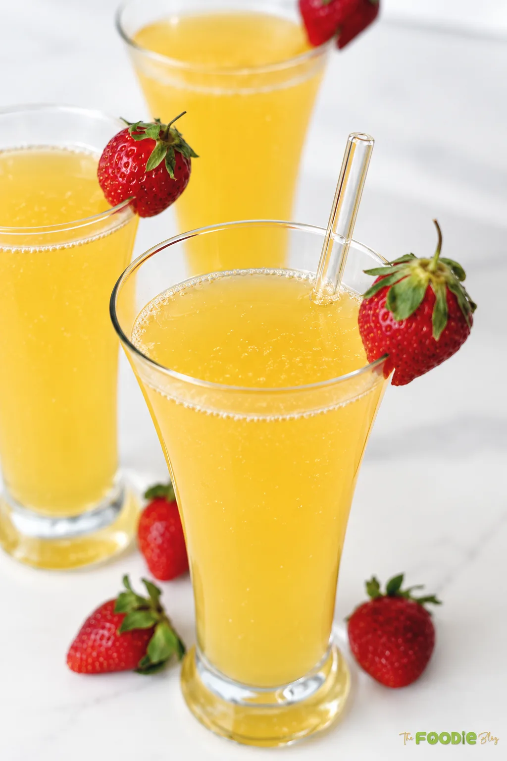 Three bubbly orange mimosas garnished with fresh strawberries.