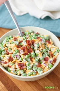 Close-up of creamy pea salad with cheddar cheese, crispy bacon, and red onion.