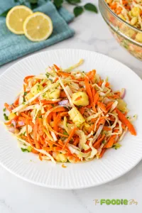 Fresh pineapple coleslaw with cabbage, carrots, red onion, cilantro, and pineapple served on a white plate.
