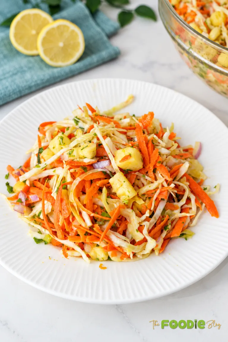 Fresh pineapple coleslaw with cabbage, carrots, red onion, cilantro, and pineapple served on a white plate.