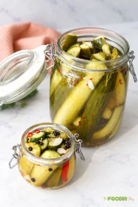 Homemade refrigerator dill pickles in two glass jars with garlic, dill, pickling spices, and red chili.