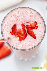 Close-up of a creamy strawberry banana smoothie topped with chopped fresh strawberries in a tall glass.