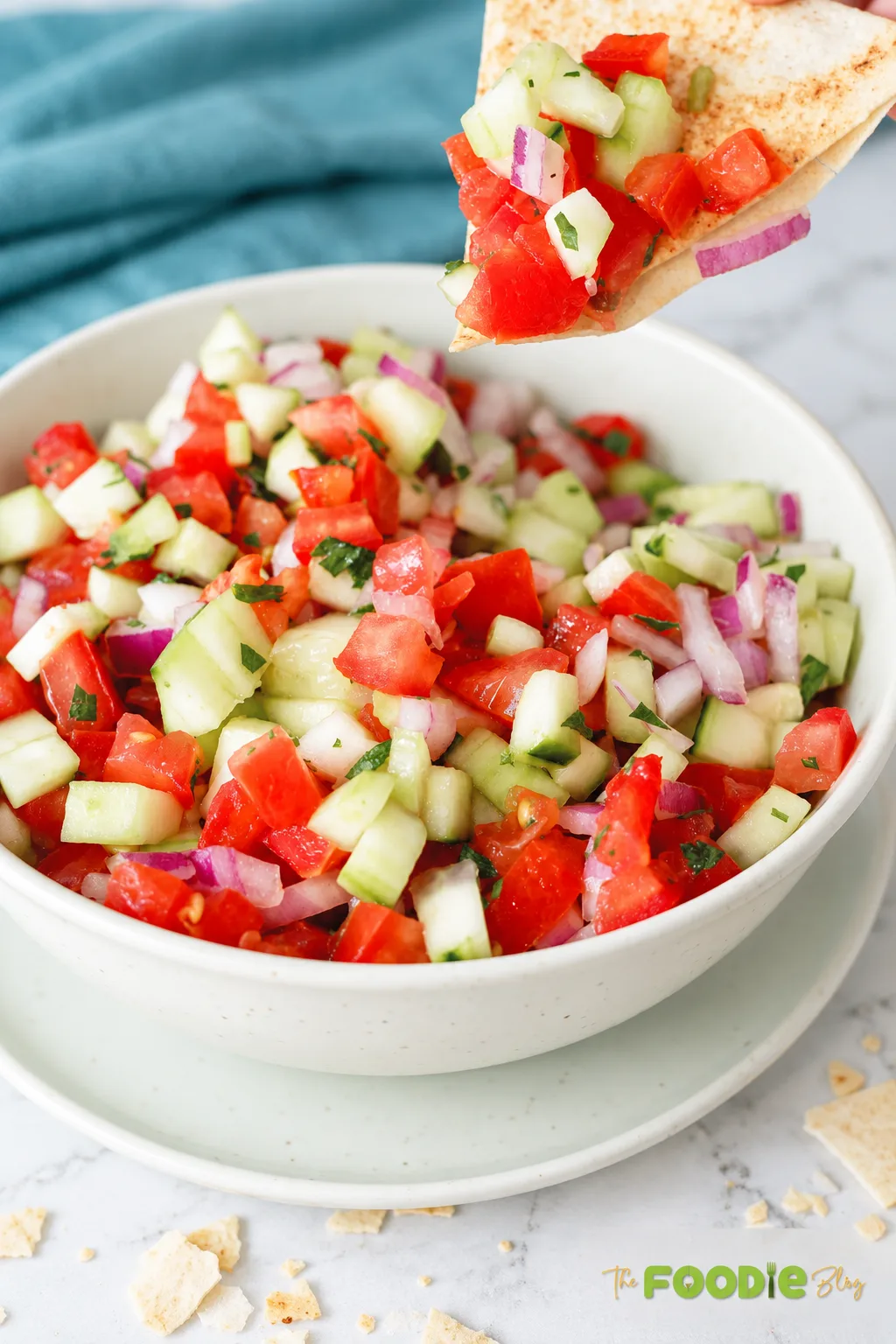 Pita bread scooping fresh tomato cucumber salad with red onion and herbs from a serving bowl.