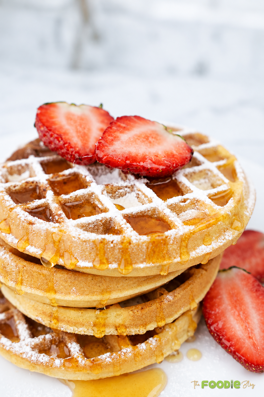 Stack of golden homemade waffles topped with strawberries, powdered sugar, and maple syrup