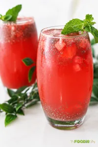 Two glasses of watermelon lemonade with basil seeds, watermelon chunks, ice, and fresh mint.