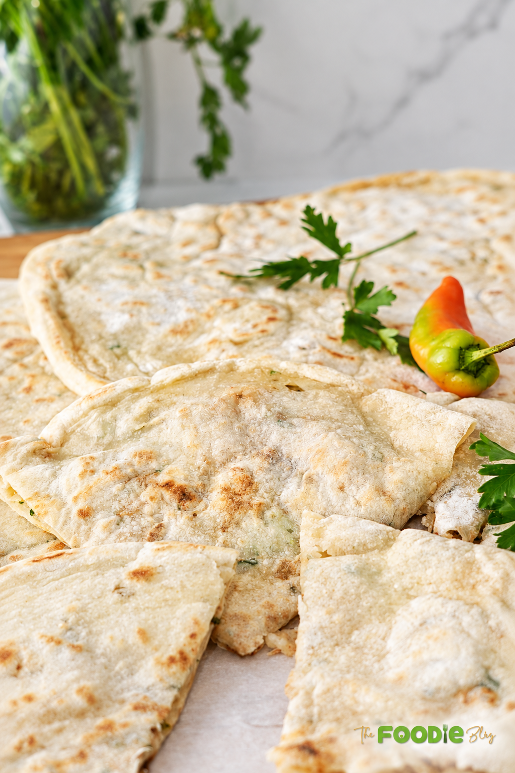 Homemade aloo paratha flatbreads stacked and folded with lightly golden surfaces, served with fresh cilantro and a pepper.