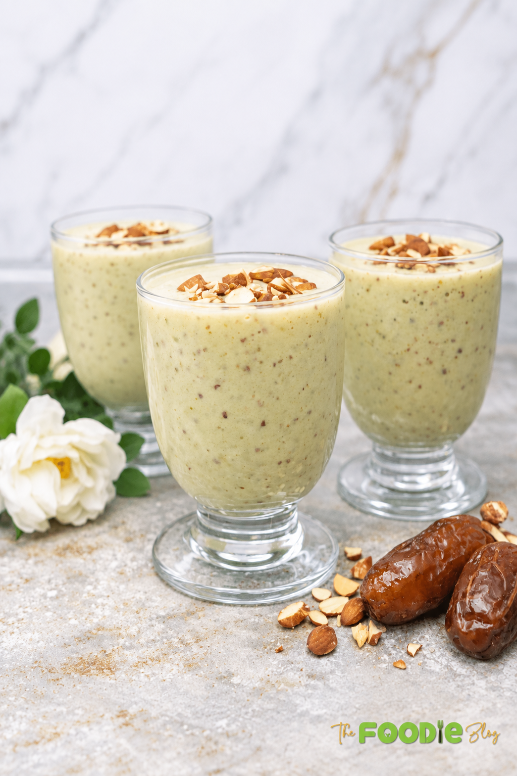Three glasses of avocado date almond drink topped with chopped almonds.