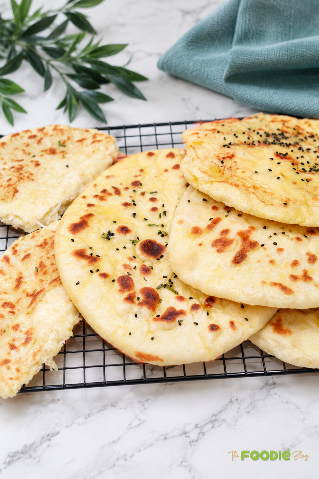 Homemade cheese naan breads stacked on a cooling rack with golden brown spots and melted cheese inside.