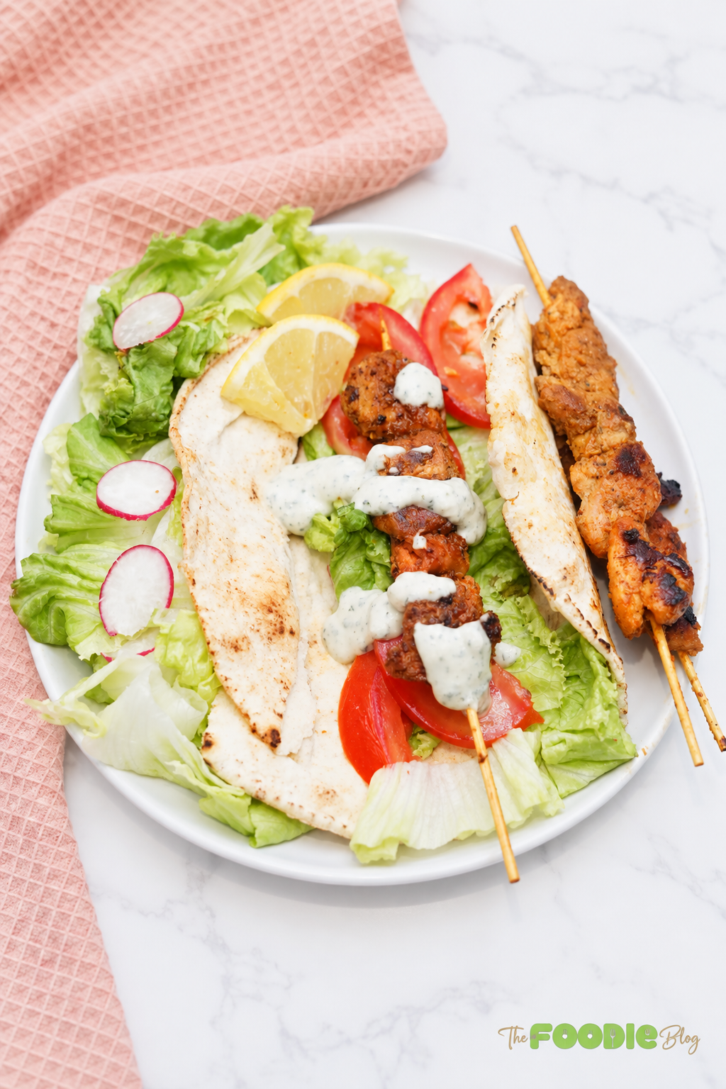 Chicken skewers served over pita bread with lettuce, tomatoes, lemon, radishes, and creamy sauce.