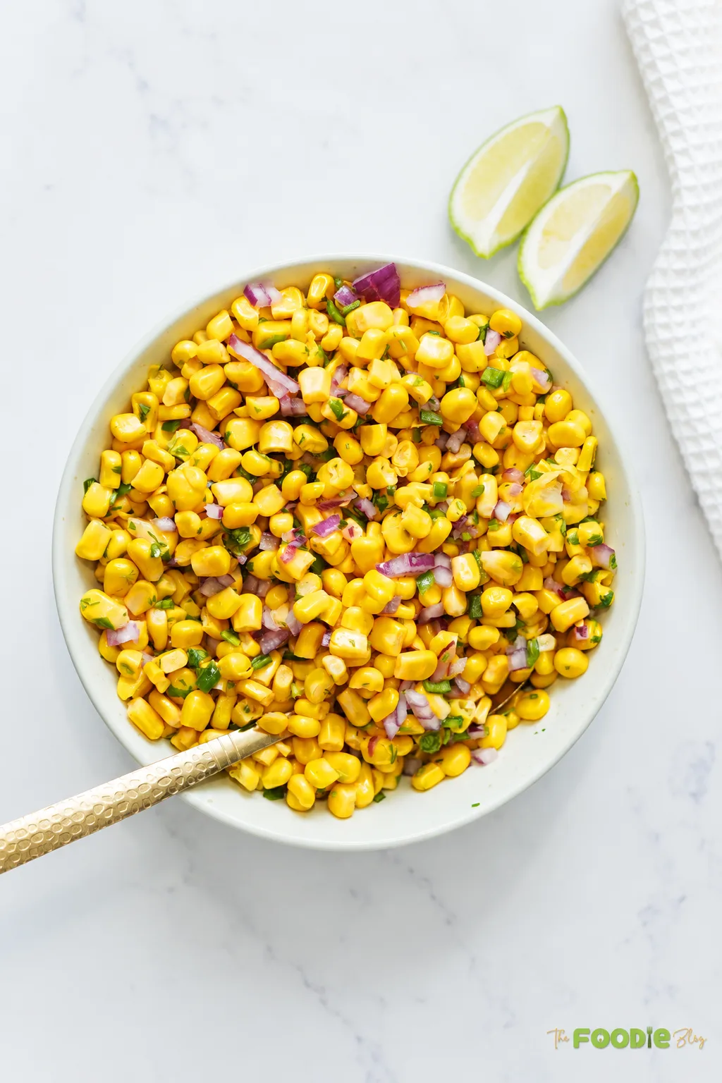 Fresh corn salsa in a bowl with red onion, jalapeño, cilantro, and lime wedges.