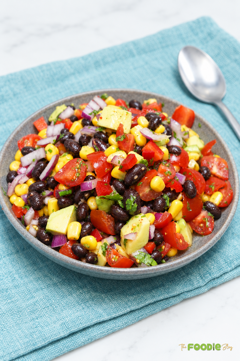 Bowl of cowboy caviar with black beans, corn, tomatoes, avocado, and red onion.
