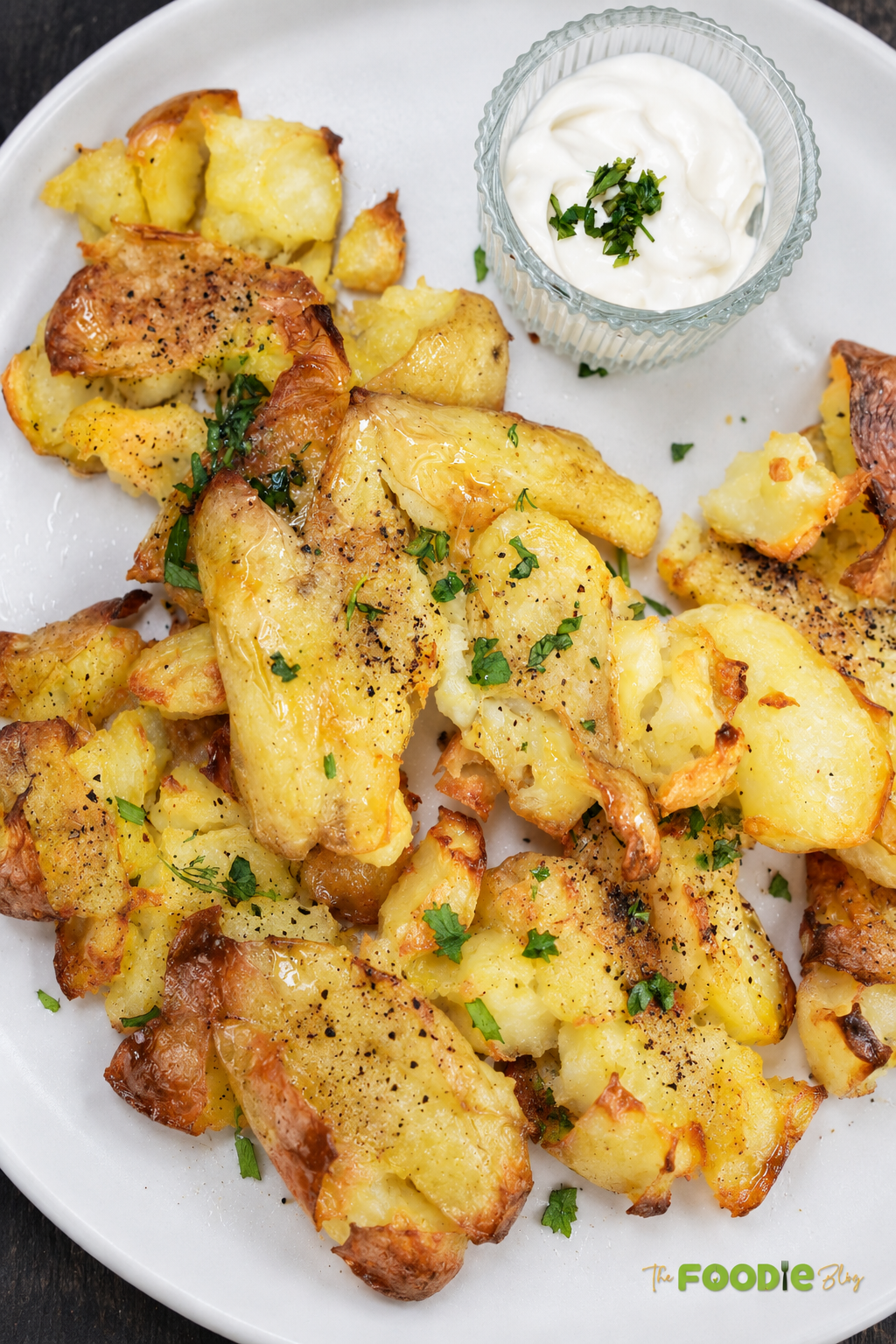 Crispy smashed potatoes served on a white plate with parsley and creamy dipping sauce.