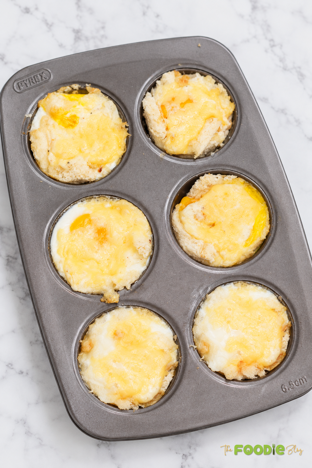 Baked Croque Madame bread cups with eggs and melted Gruyere cheese in a muffin tin.