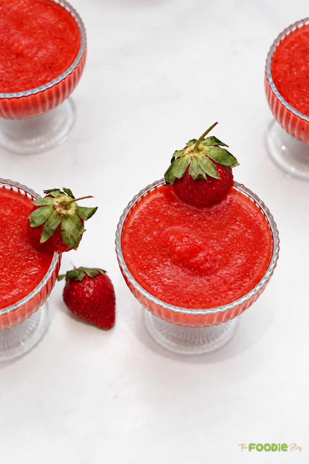 Four frozen strawberry daiquiris served in glass cups with fresh strawberry garnish.