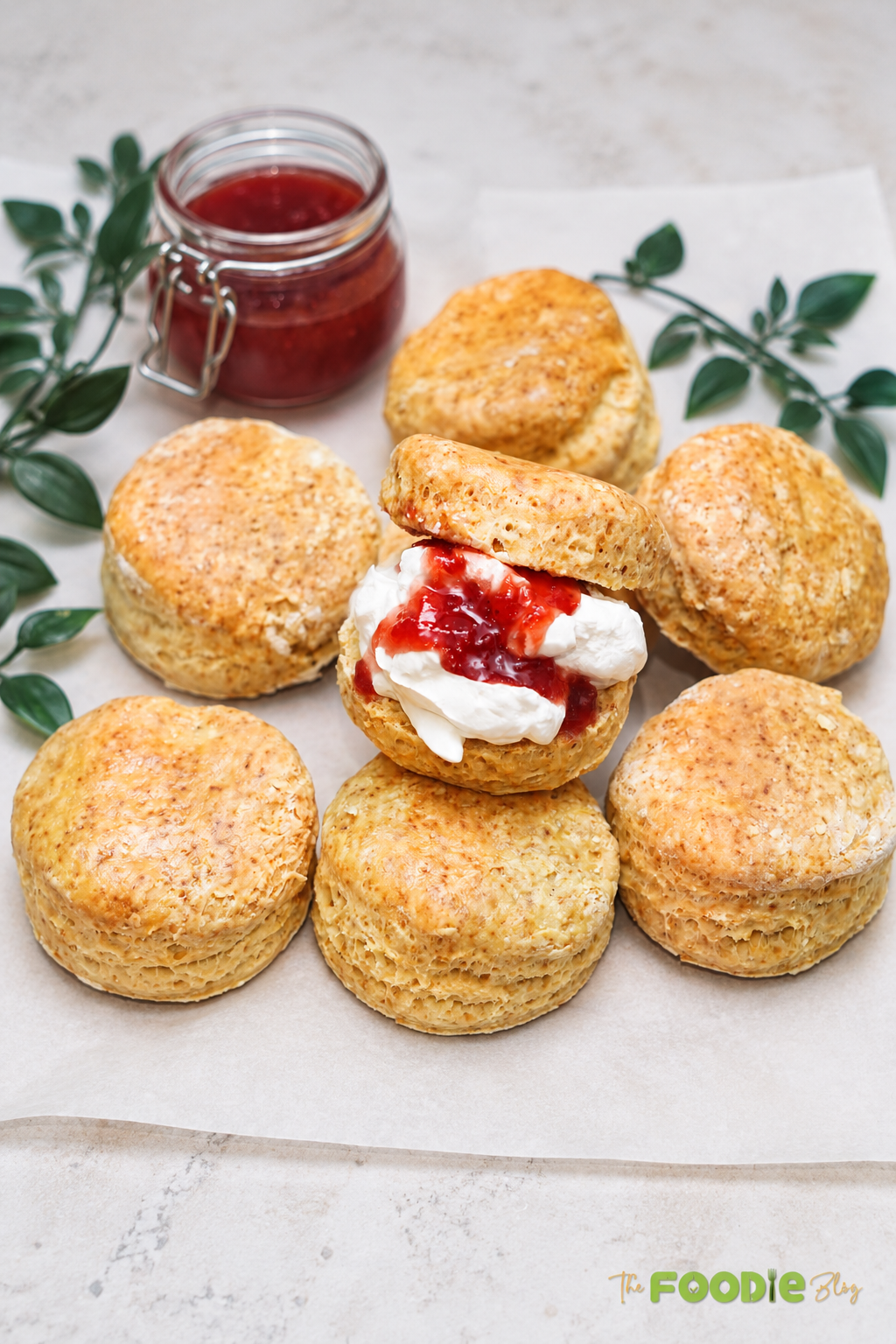 Freshly baked English scones with one scone filled with whipped cream and strawberry jam.