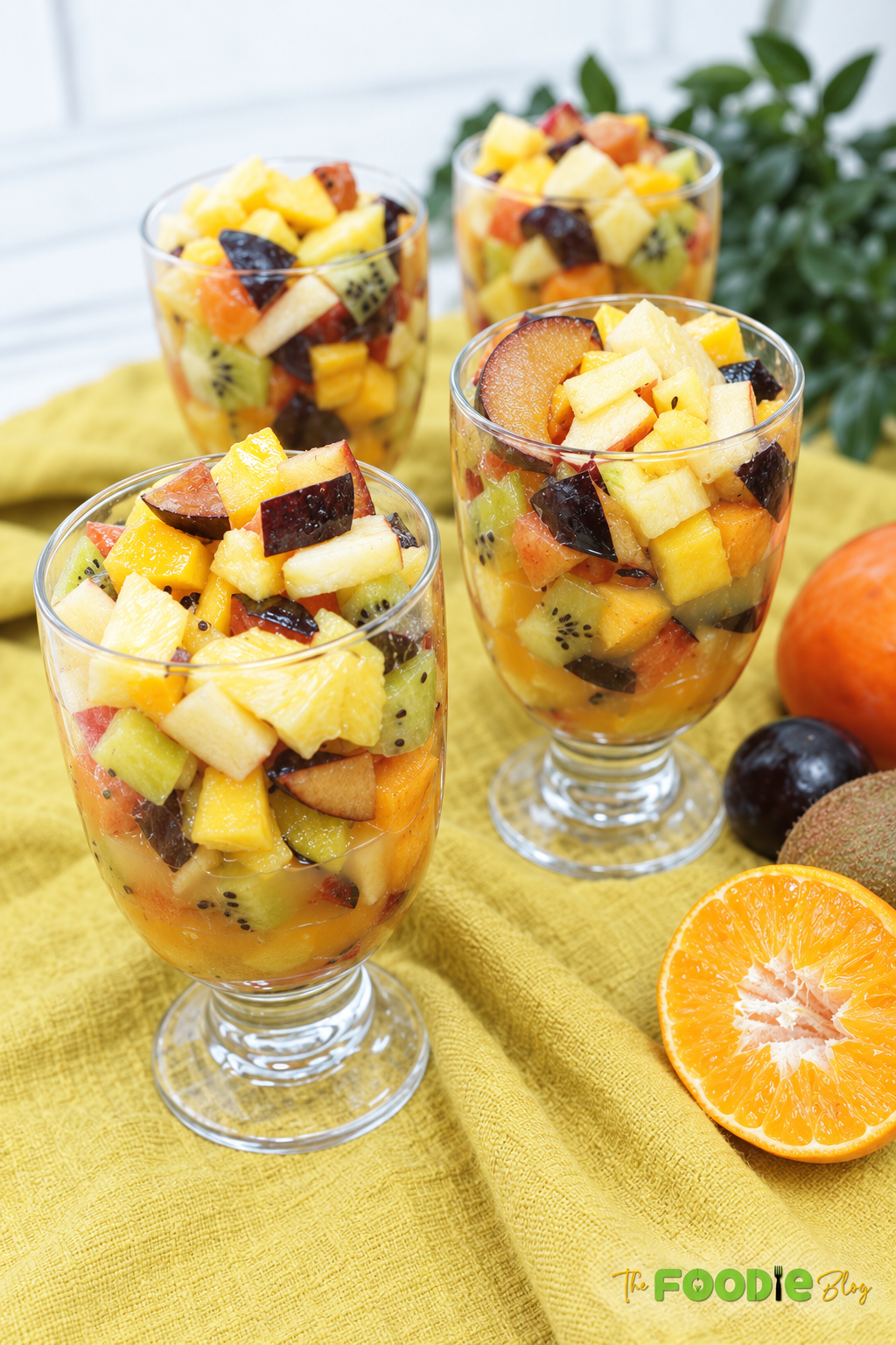 Four glasses filled with colorful fresh fruit salad made with pineapple, mango, kiwi, plums, apples, and persimmons.