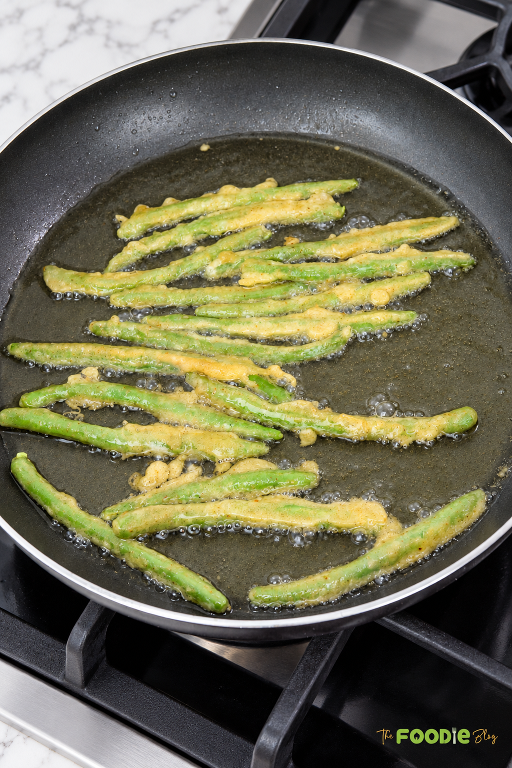 Battered green beans frying in hot oil in a skillet until crispy.