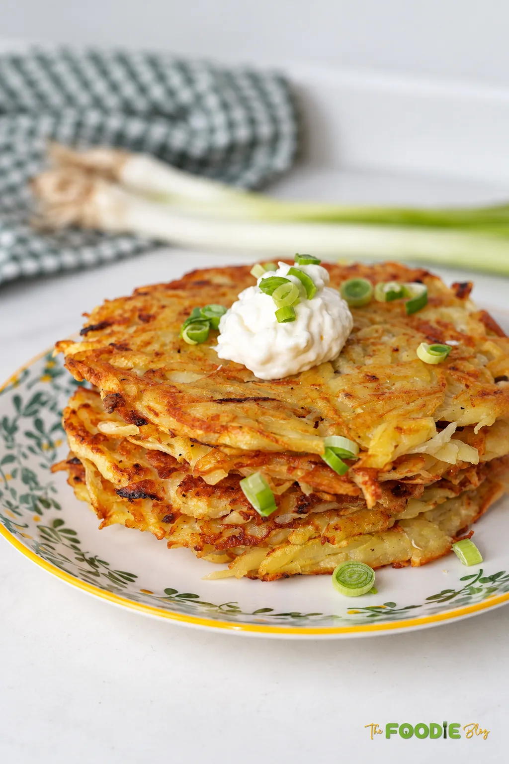 Stack of homemade German potato pancakes topped with sour cream and chopped green onions.