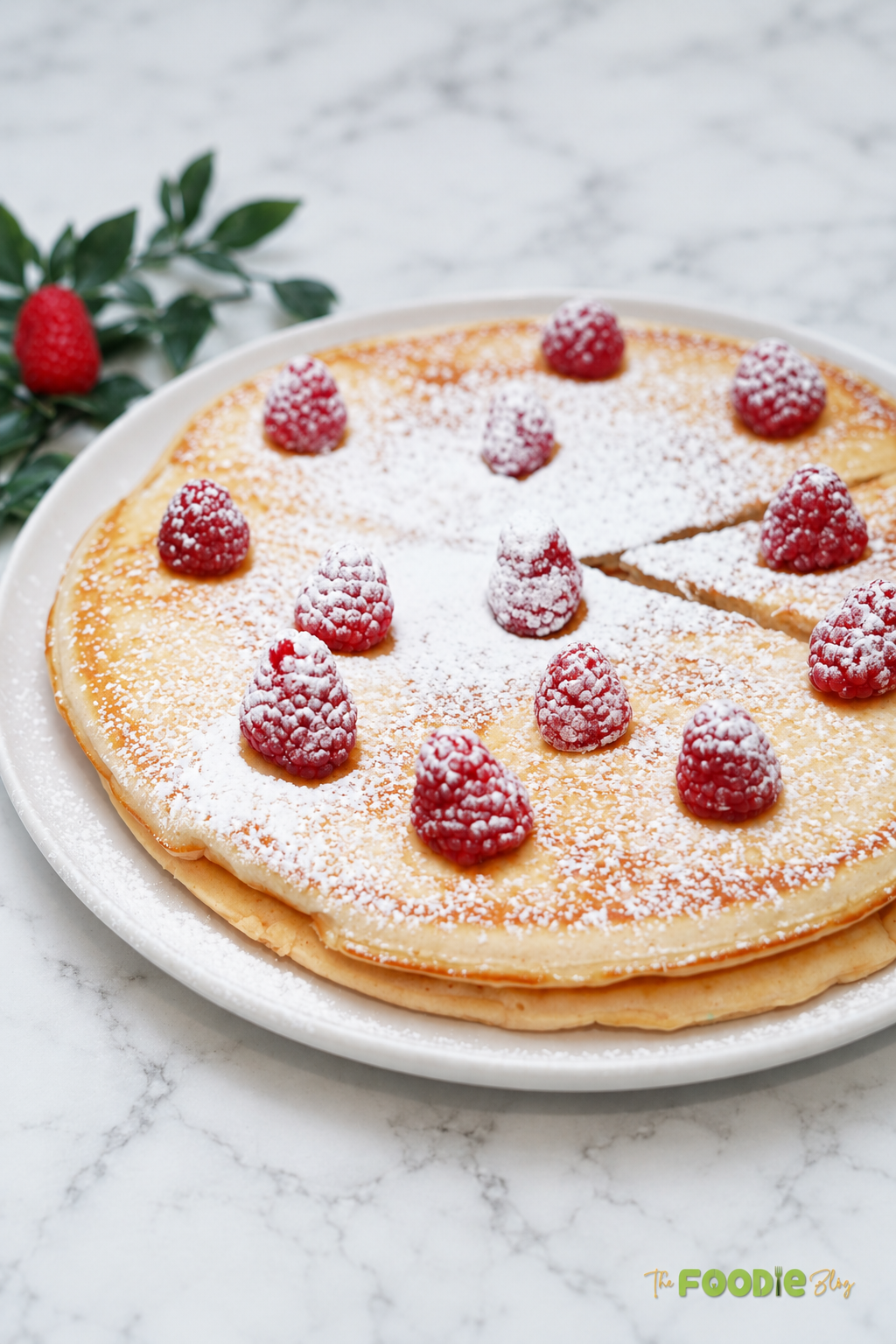 Stack of giant fluffy pancakes topped with raspberries and powdered sugar.