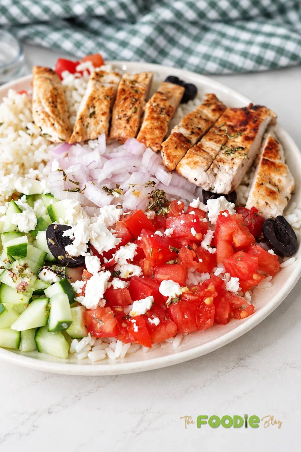 Close-up Greek chicken rice bowl topped with sliced grilled chicken, tomatoes, cucumber, feta, red onion, and olives.