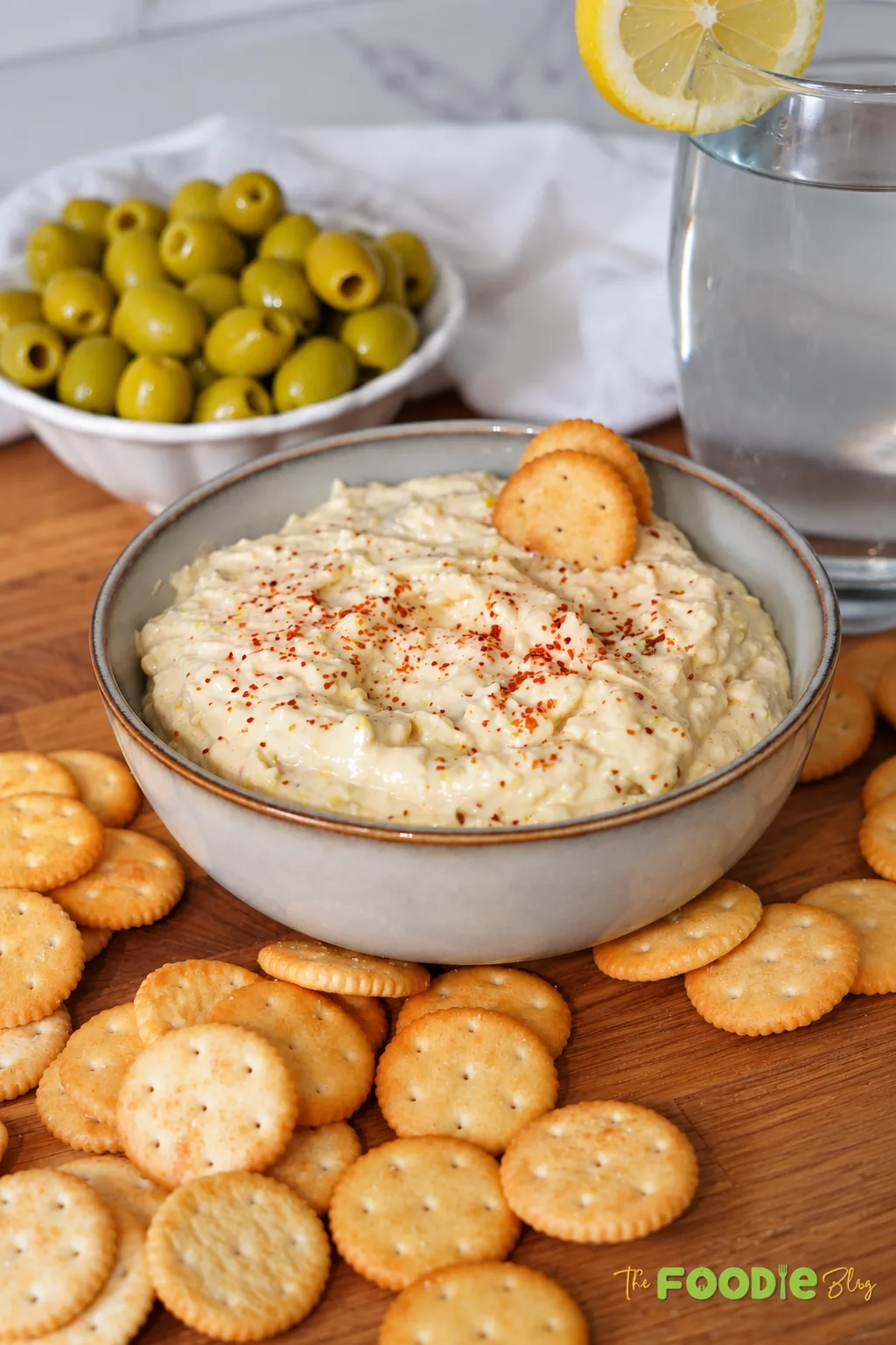 Creamy green olive dip topped with paprika and served with crackers and green olives.