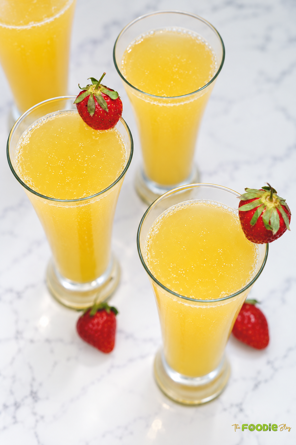 Three glasses of orange juice and Prosecco cocktails with strawberry garnishes.