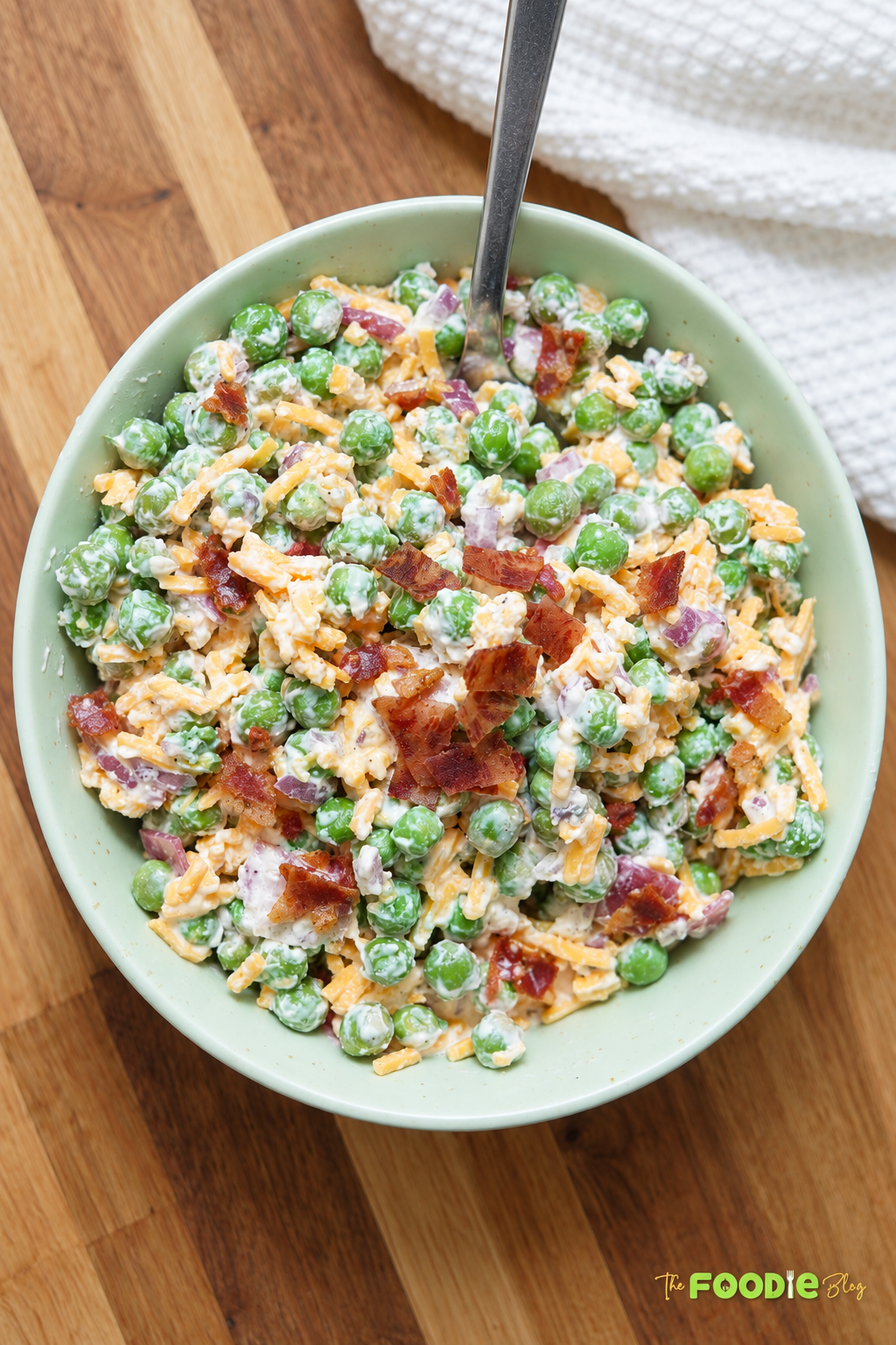 Creamy pea salad with green peas, cheddar cheese, bacon, and red onion in a serving bowl.