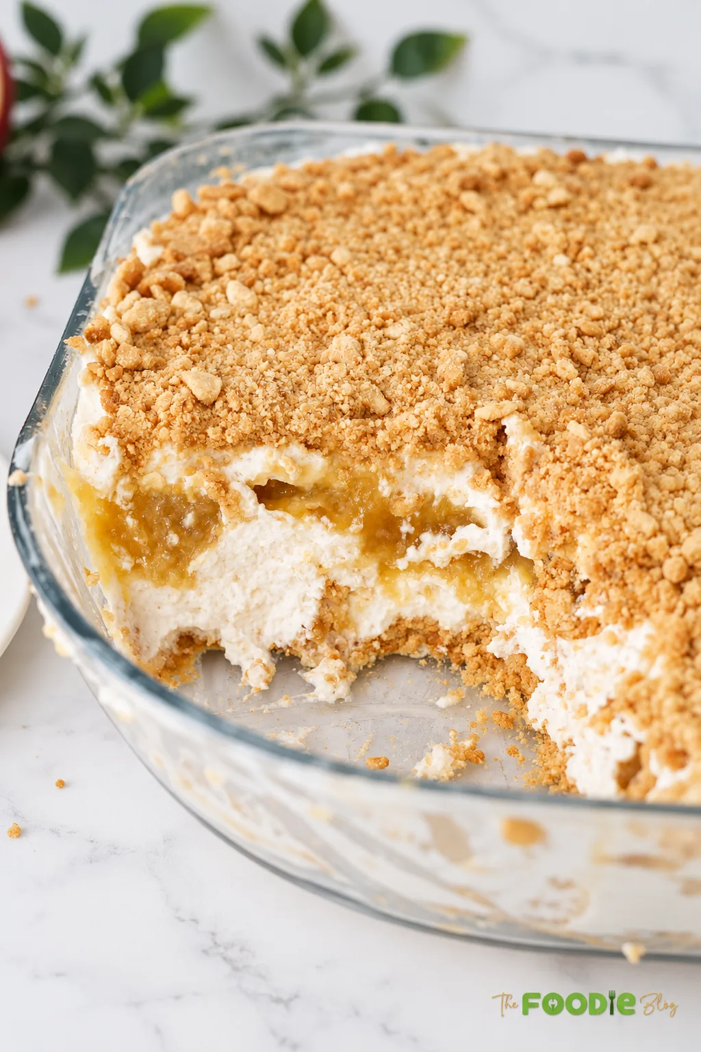 No-bake peach dessert in a glass dish with a portion removed showing creamy peach layers and biscuit crumbs.