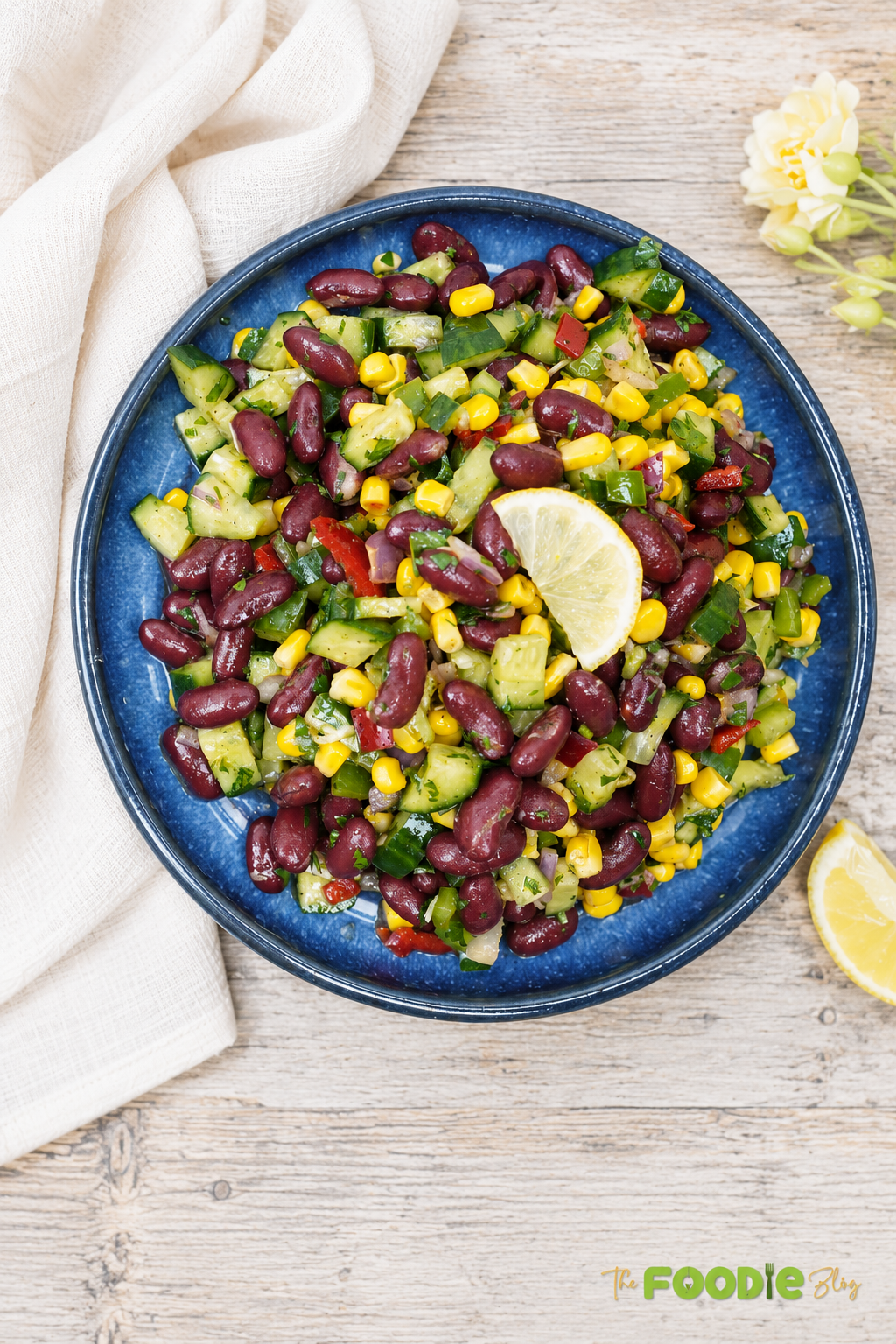 Red bean salad served in a blue bowl with corn, cucumber, bell peppers, parsley, and lemon.