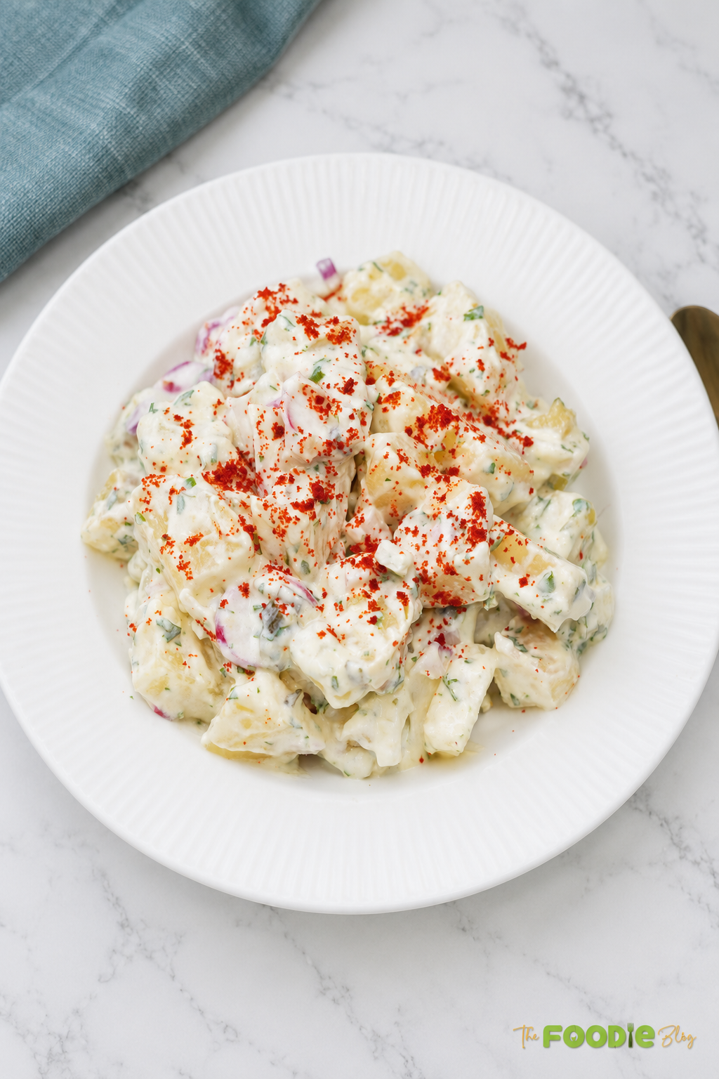 Homemade red potato salad served on a white plate and sprinkled with smoked paprika.