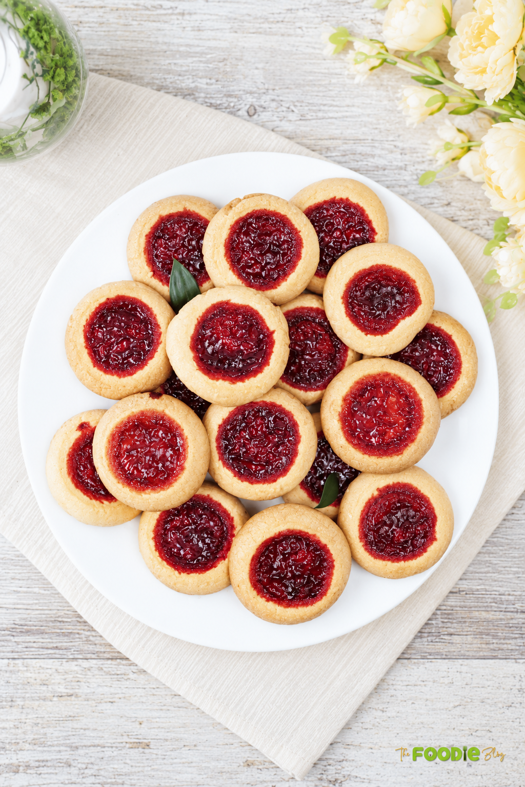 Overhead view of strawberry jam shortbread cookies arranged on a white serving plate.