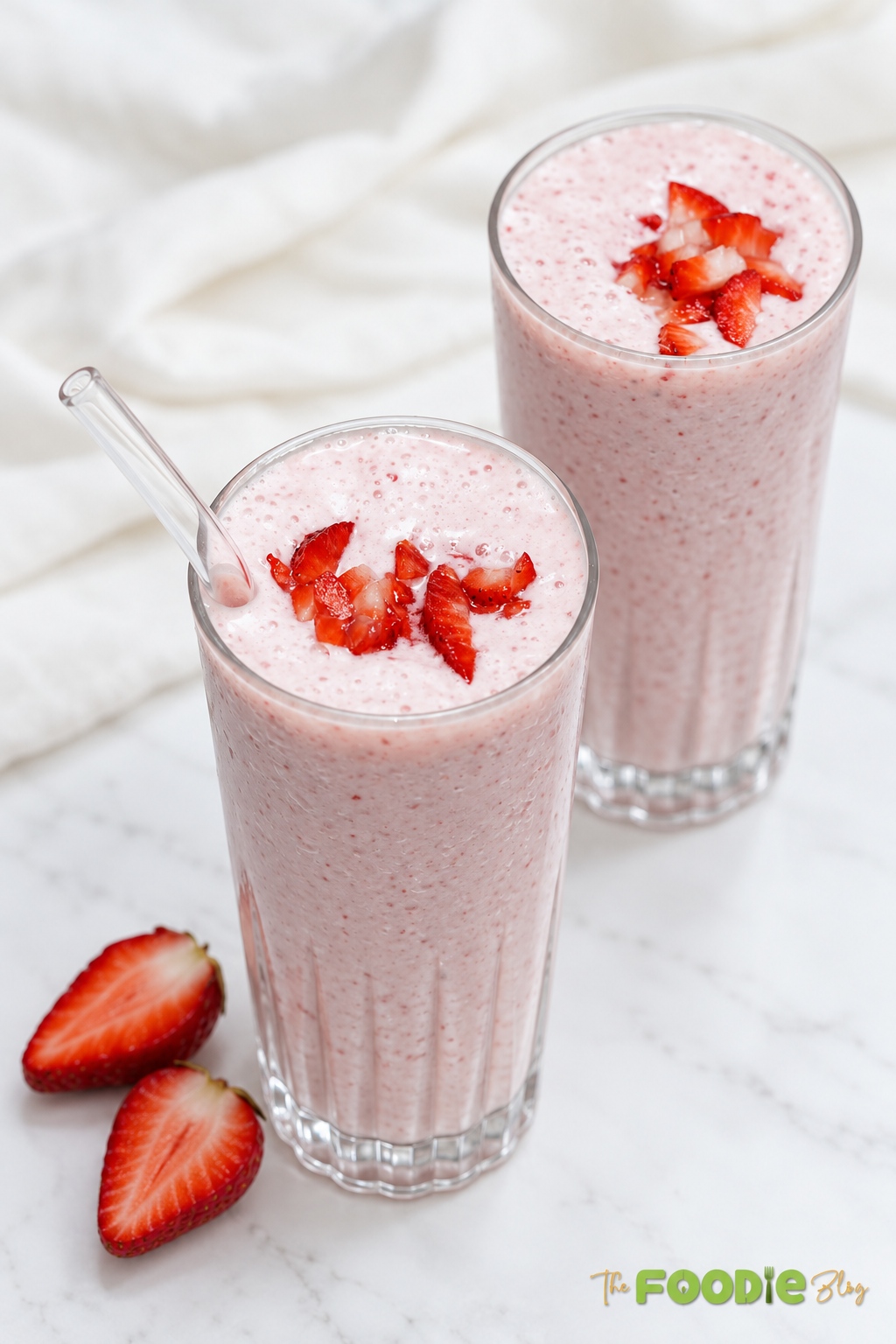 Two tall glasses of creamy strawberry banana smoothie topped with chopped strawberries.